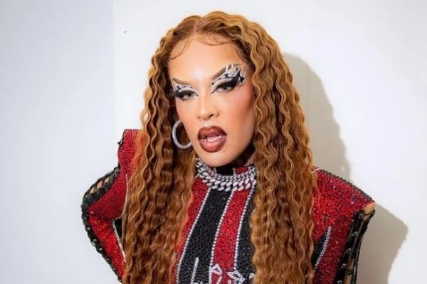 Gloria Groove contou uma história inusitada em sua participação no programa Que História É Essa, Porchat?, do canal Multishow, na última terça-feira, 26. A drag queen revelou que se "livrou" do enquadro de um policial armado após ele a reconhecer por cantar com Ludmilla. A situação aconteceu durante uma viagem de carro de São Paulo para o Rio de Janeiro, quando Gloria estava desmontada e, portanto, era Daniel Garcia, o seu nome verdadeiro quando não está sendo a drag queen. Ele estava dormindo no banco de trás com o seu motorista, Davi, dirigindo. Quando acordou, o carro estava sendo abordado por policiais. "Quando eu abri o olho, a cena era: o vidro do Davi aberto, o meu também e tinha a Polícia Militar do Rio de Janeiro com uma metralhadora dentro do carro", disse. Como Daniel não estava "montado", o policial não reconheceu que ele era Gloria Groove. Nisso, ele precisou cantar um trecho da música Vermelho e até mostrar uma foto do celular e provar que era a drag queen comparando as tatuagens de seu corpo Ainda assim, o policial só se tranquilizou quando o associou ao nome de Ludmilla. "Ele deu uma pausa muito dramática, olhando para a minha cara e falou: ‘Gloria Groove que canta com a Ludmilla?’ Aí, enfim... ficou tudo bem", contou. "O jeito que foi de 0 a 100 foi absurdo. Fiquei na mira de uma arma na maior parte do tempo e quando a Ludmilla era minha amiga [ficou tudo bem]. Fica a conclusão: às vezes, ter o contato certo é muito mais importante do que qualquer outra coisa", brincou.